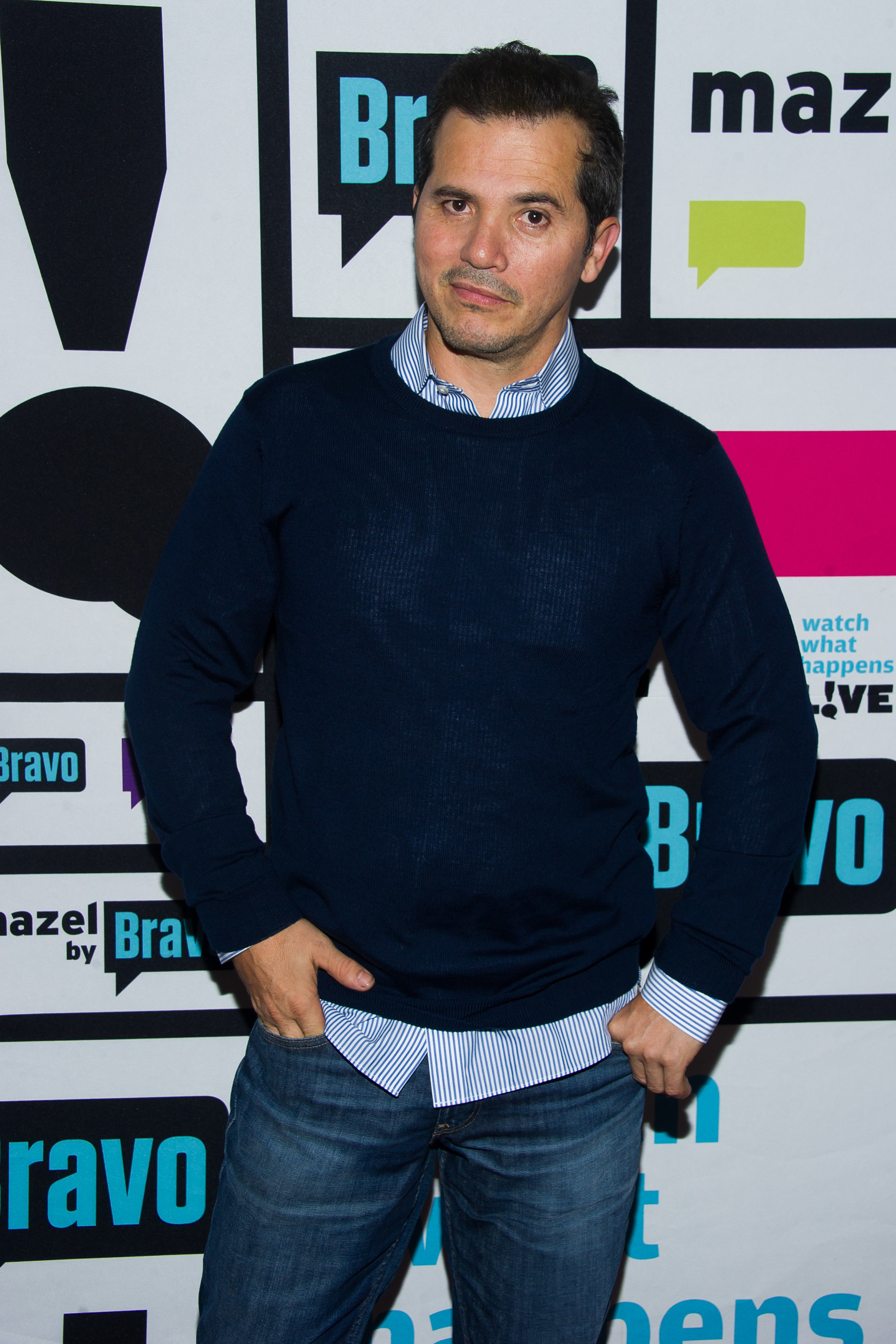 John Leguizamo poses in a dark sweater and jeans at an event for "Watch What Happens Live" by Bravo