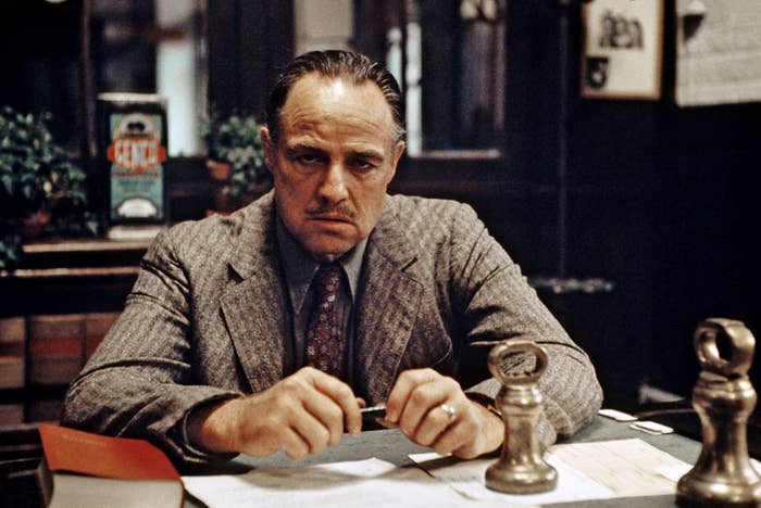 Marlon Brando as Vito Corleone, dressed in a suit, sitting at a desk in a scene from "The Godfather"