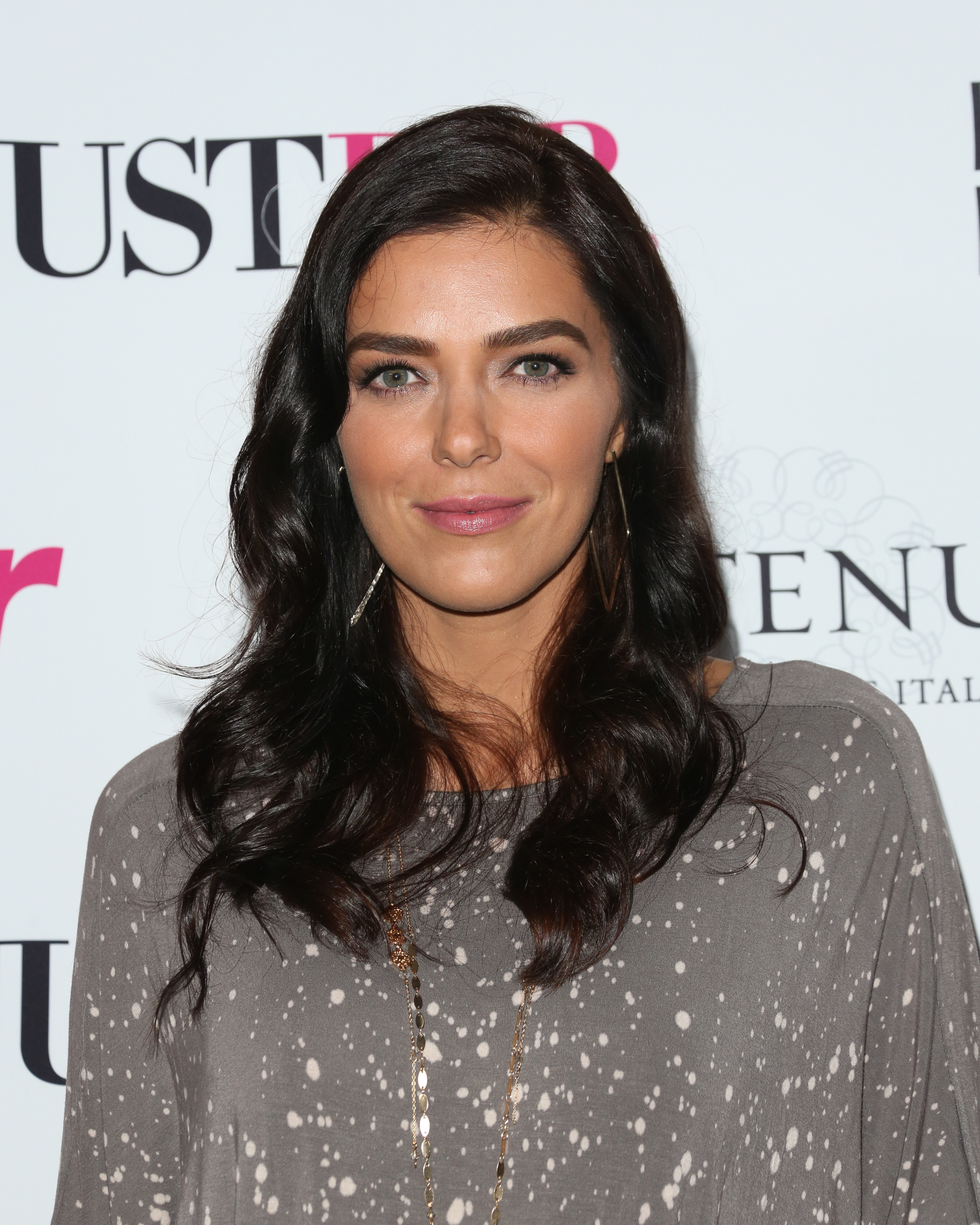 Adriana Lima at a red carpet event, wearing a casual speckled grey top with minimal jewelry