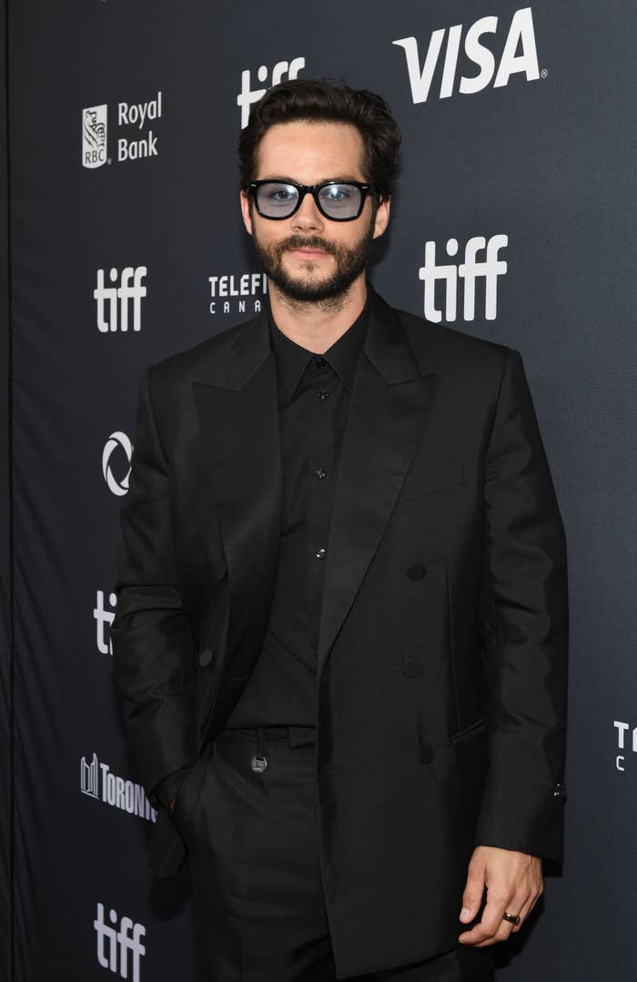 Dylan O’Brien on the red carpet at TIFF, wearing a stylish dark suit and sunglasses, posing for photos