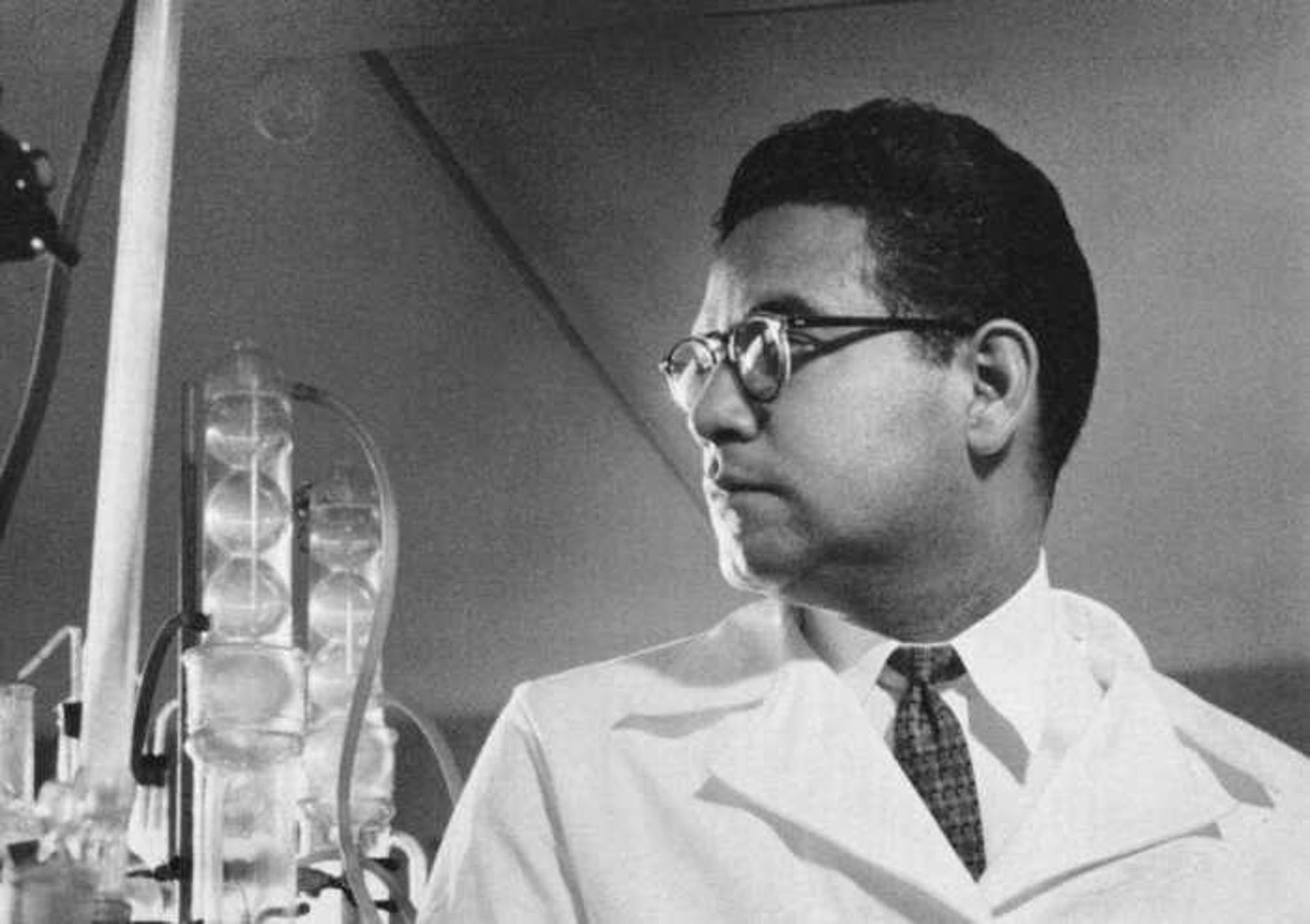 Luis Miramontes in a laboratory wearing a white lab coat and a tie, looking to the side