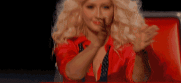 Christina Aguilera, seated, claps her hands enthusiastically during a TV show