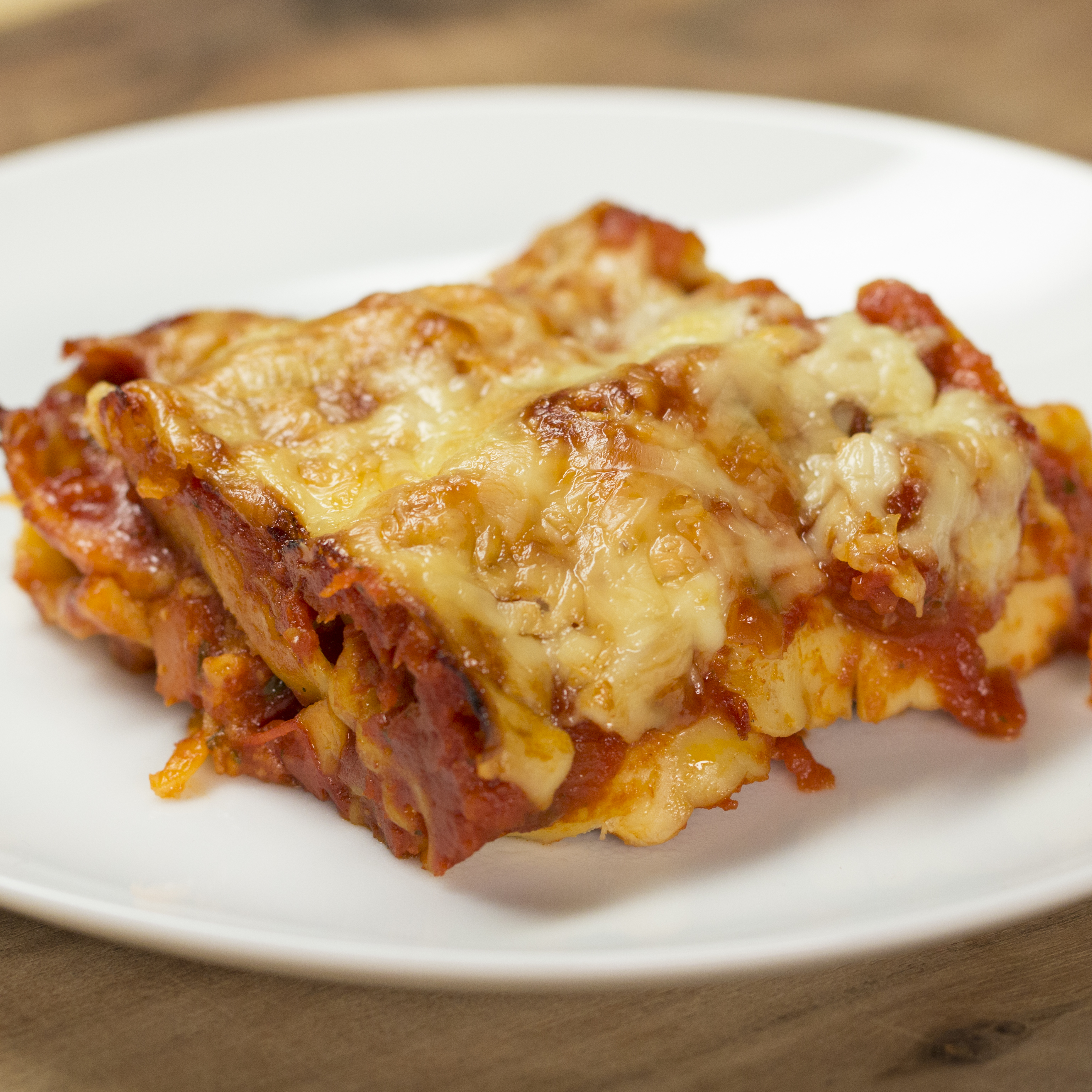 A slice of lasagna on a white plate, showcasing layers of pasta, cheese, and tomato sauce