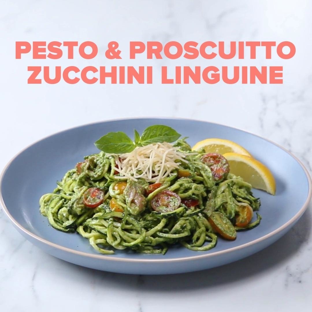 Plate of zucchini linguine topped with pesto, prosciutto, cherry tomatoes, and a garnish of cheese and basil, served with lemon wedges. Text: &quot;Pesto &amp;amp; Prosciutto Zucchini Linguine.&quot;
