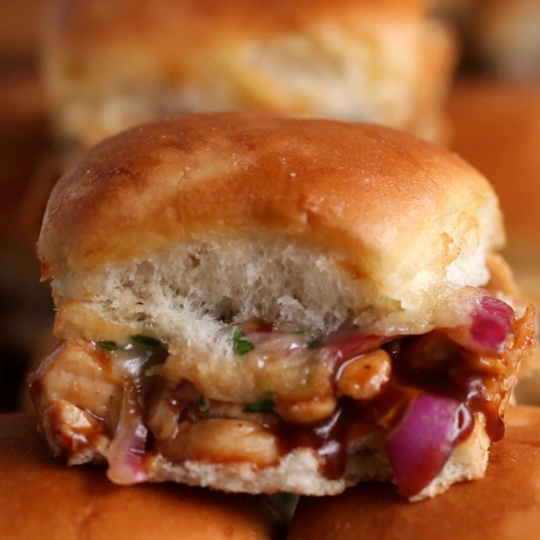 Close-up of a slider sandwich with chicken, barbecue sauce, onions, and herbs. The article is categorized under Tasty