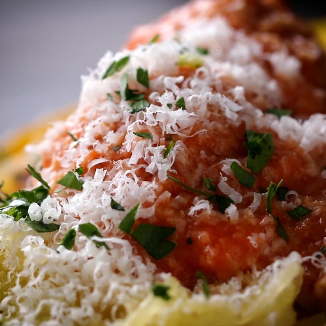 Close-up of a plate of pasta topped with tomato sauce, grated parmesan cheese, and garnished with fresh parsley