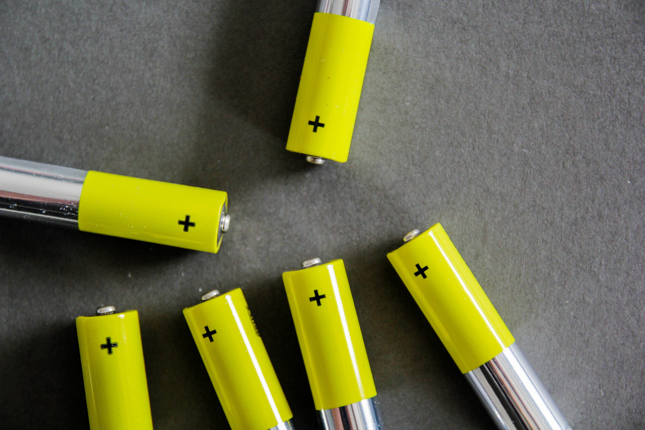 Close-up of several yellow batteries with plus signs indicating the positive terminals, scattered on a flat surface