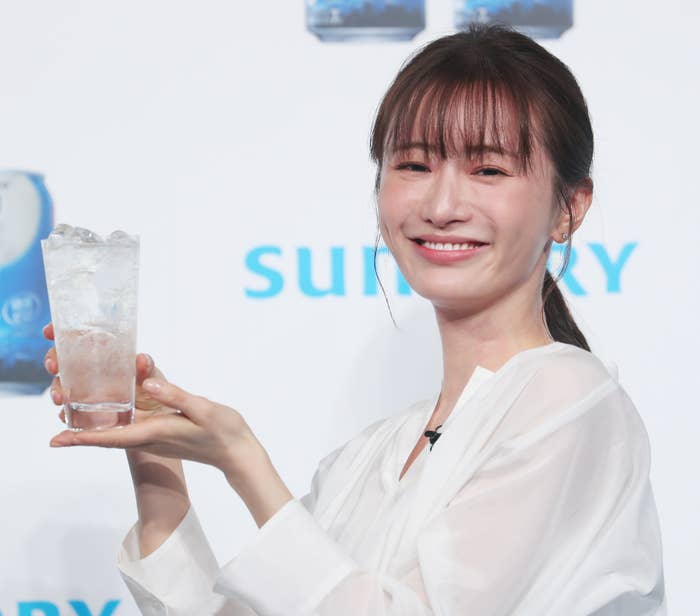 女性モデルが一杯の炭酸飲料を持ち笑顔でカメラに向かっている。背景には「サントリー」のロゴが見える。