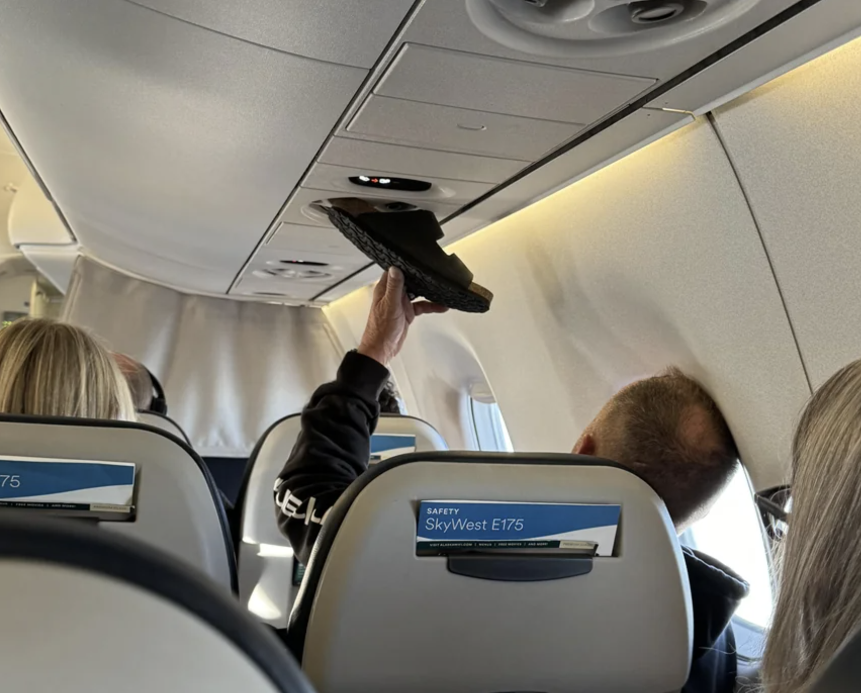 Person places shoe into airplane overhead bin above their seat during a flight