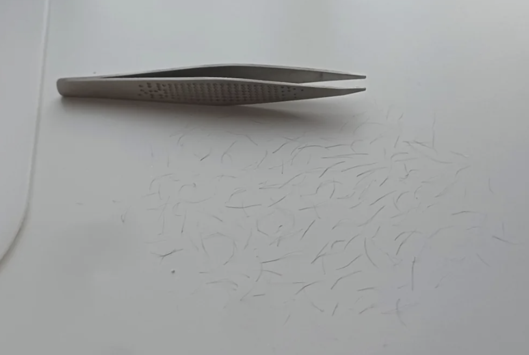 Tweezers resting on a white surface with many small hair clippings scattered around