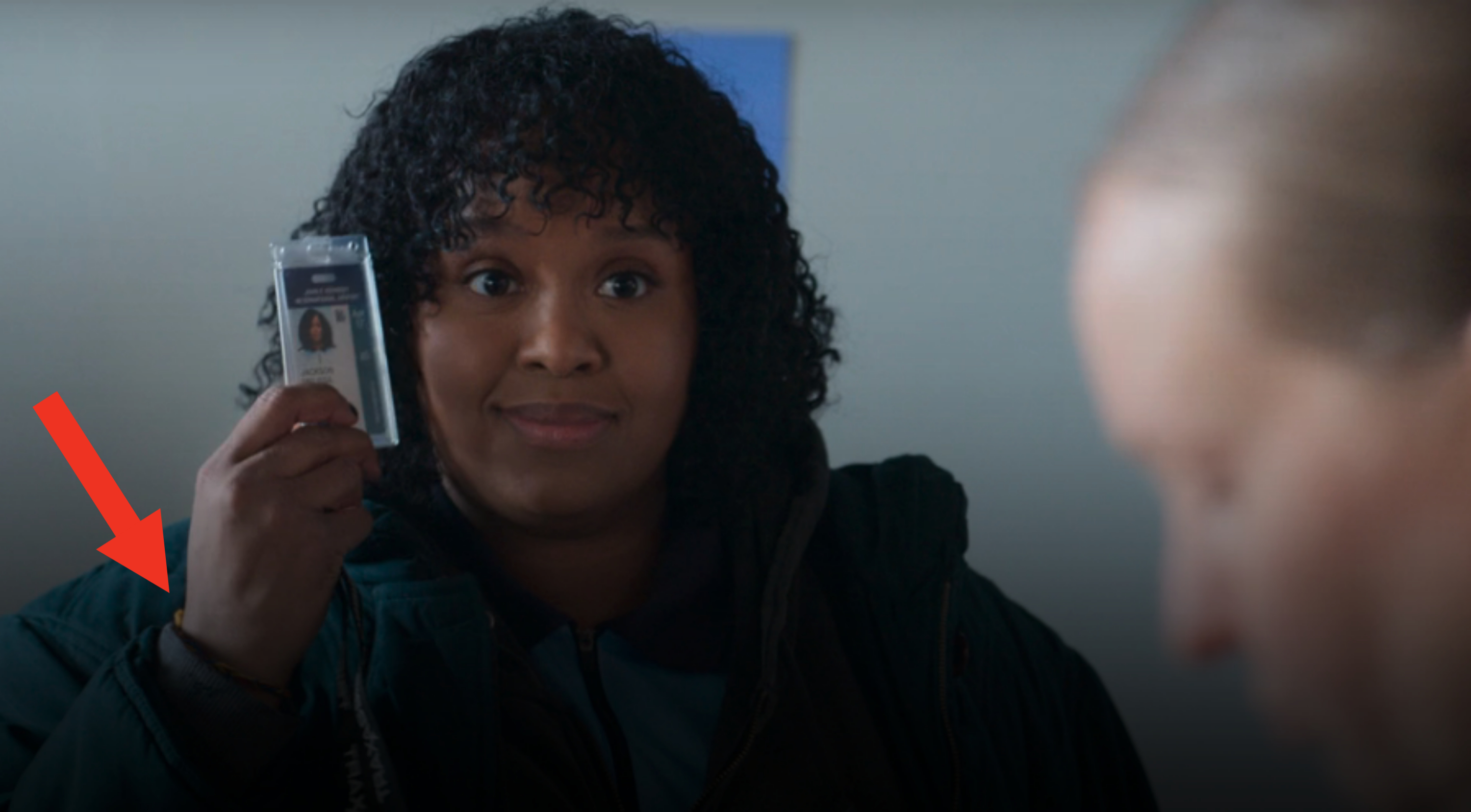 Natasha Rothwell holds up an ID badge while looking at another person in the image