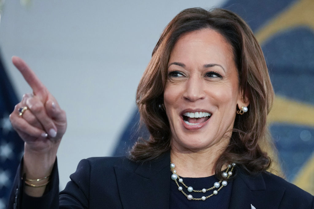 Kamala Harris smiles and points while dressed in a stylish suit with layered pearl necklaces