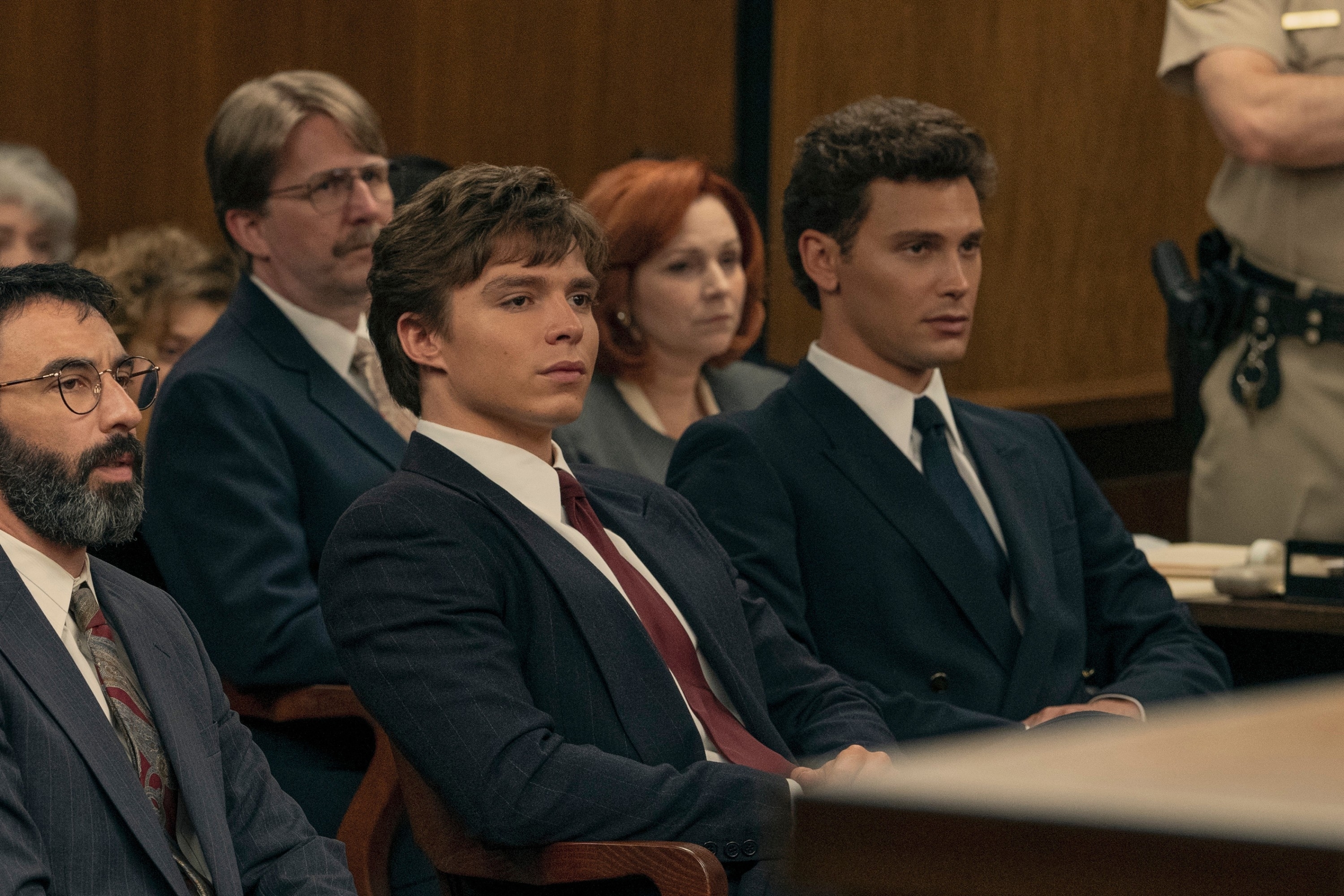 Group of people in a courtroom, including Ansel Elgort and Josh Duhamel, who are seated and dressed in formal suits