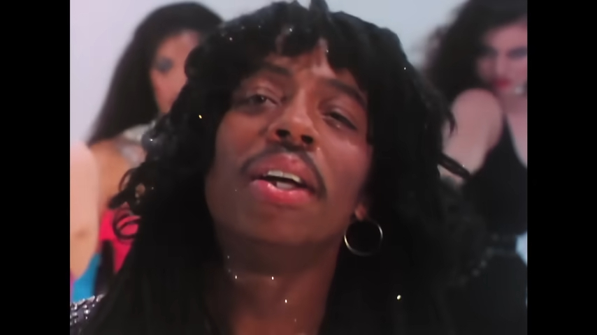 Rick James with shoulder-length hair sings with several background dancers