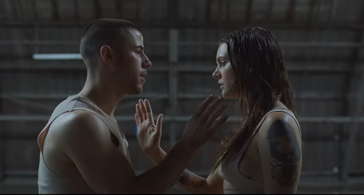 Nick Jonas and a woman in an intimate moment, facing each other with raised hands, wearing casual sleeveless shirts