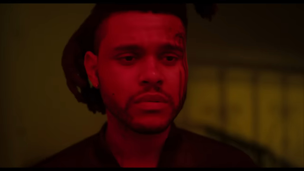 The Weeknd gazes pensively in a dimly lit setting, his facial expression serious, suggesting deep thought or emotion