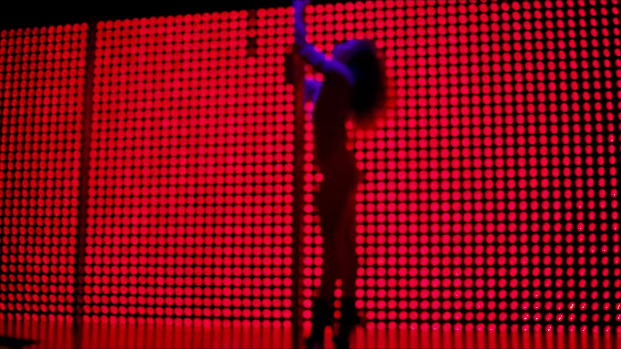 A person in silhouette performs on a pole against a backdrop illuminated with a grid of circular lights