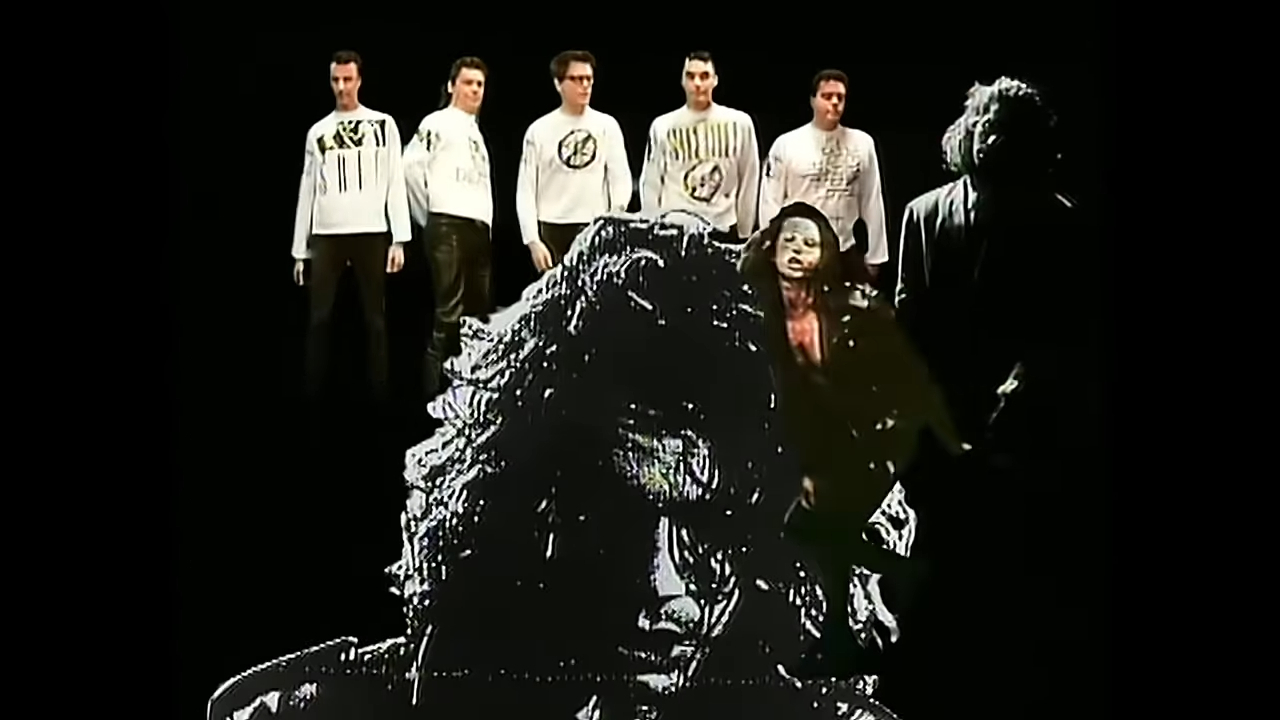Six men wearing graphic sweatshirts pose in front of an image of a man with long curly hair.