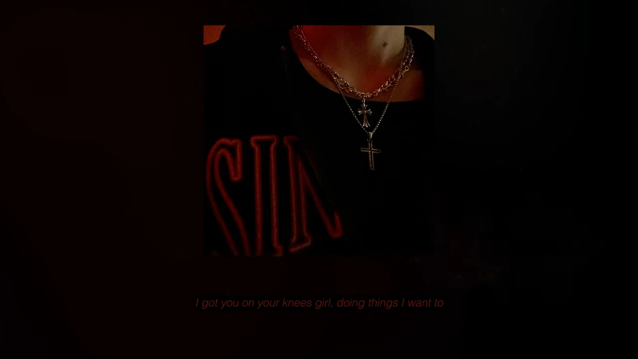 A close-up of a person's neck wearing multiple silver chains with a cross pendant. Text at the bottom reads: "I got you on your knees girl, doing things I want to."