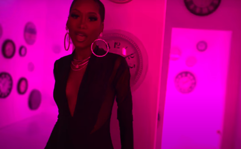 A fashionable person in a modern setting with multiple clocks on the walls. The image is bathed in pink lighting