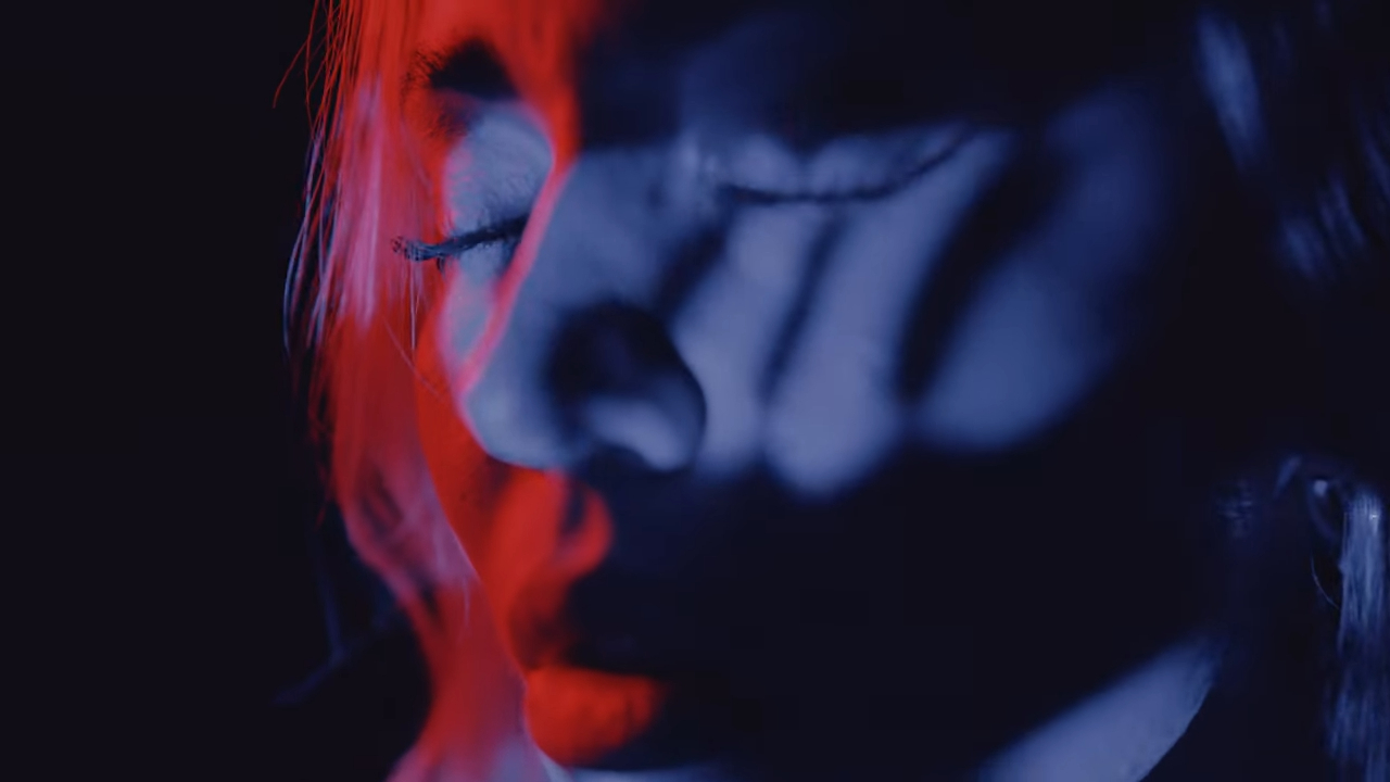 Close-up of a woman's face with closed eyes, partially obscured by shadows and red light. Sensual and moody atmosphere