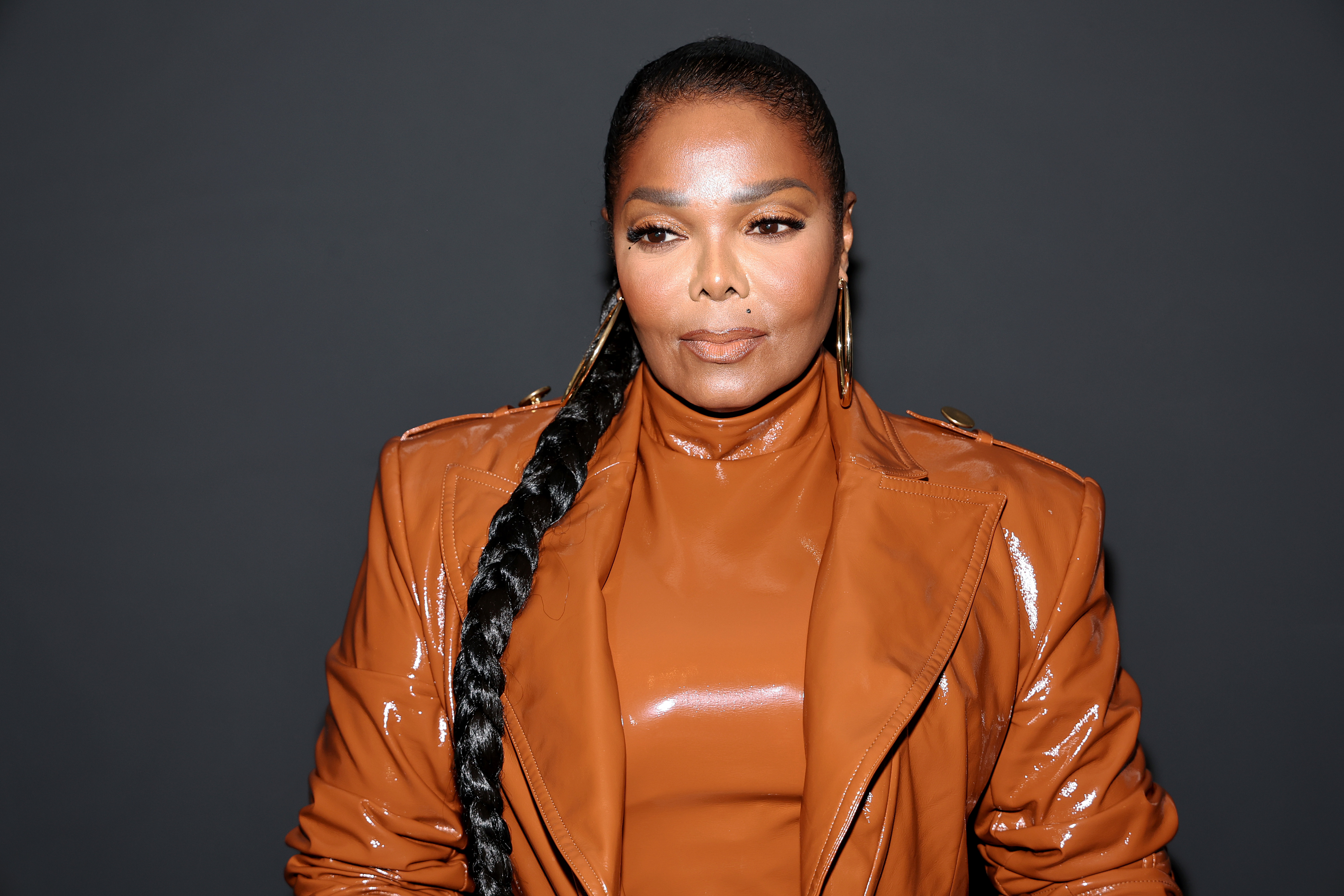 Janet Jackson is wearing a glossy leather jacket with matching turtleneck and long braided ponytail
