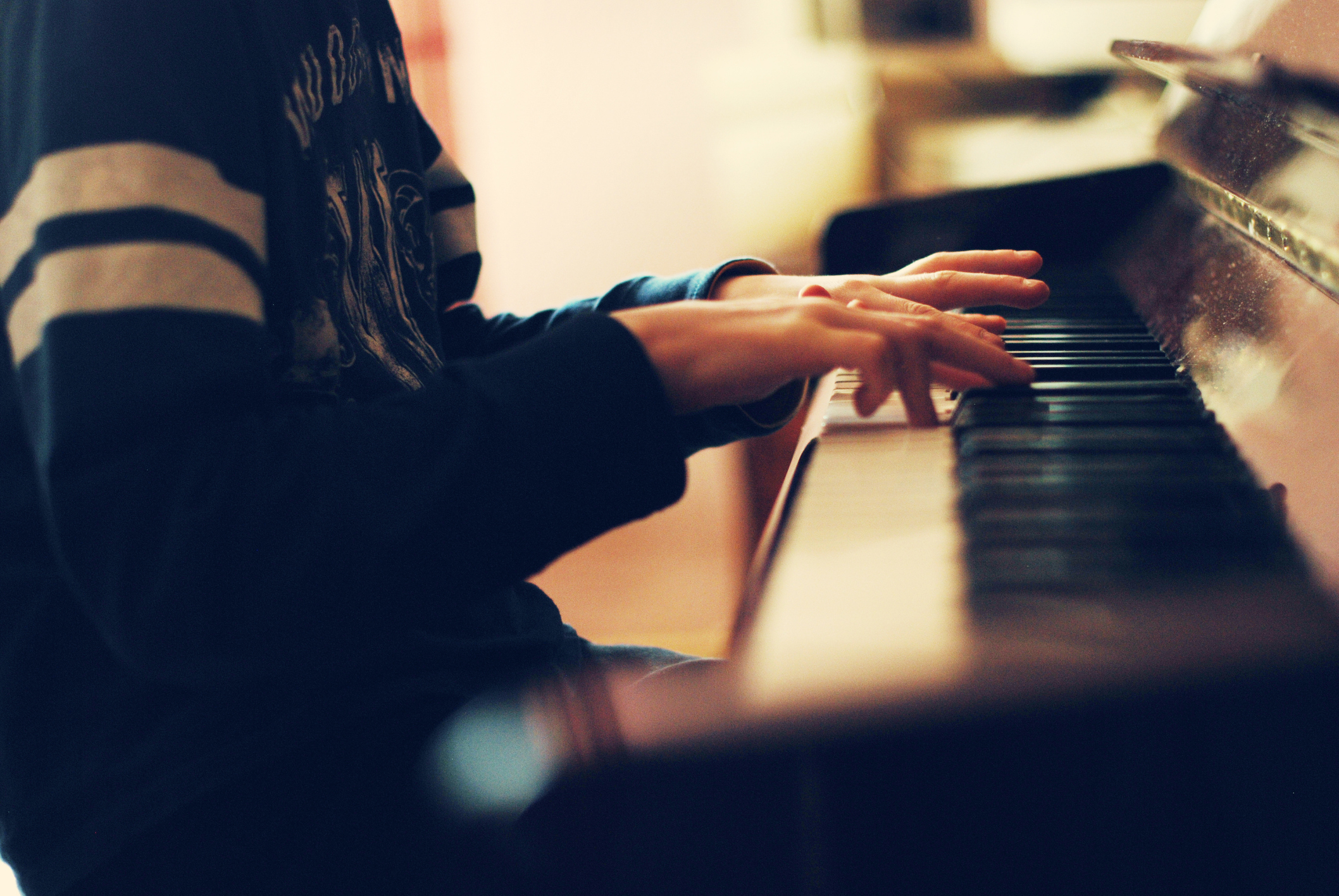 Person playing the piano with focused hands on the keyboard. The person's face is not visible