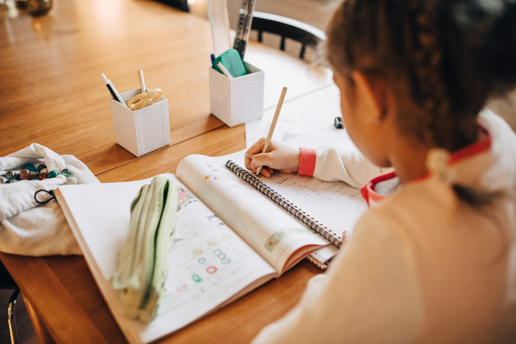 Child doing homework at a wooden table with pencils, a ruler, and drawing cats in a sketchbook