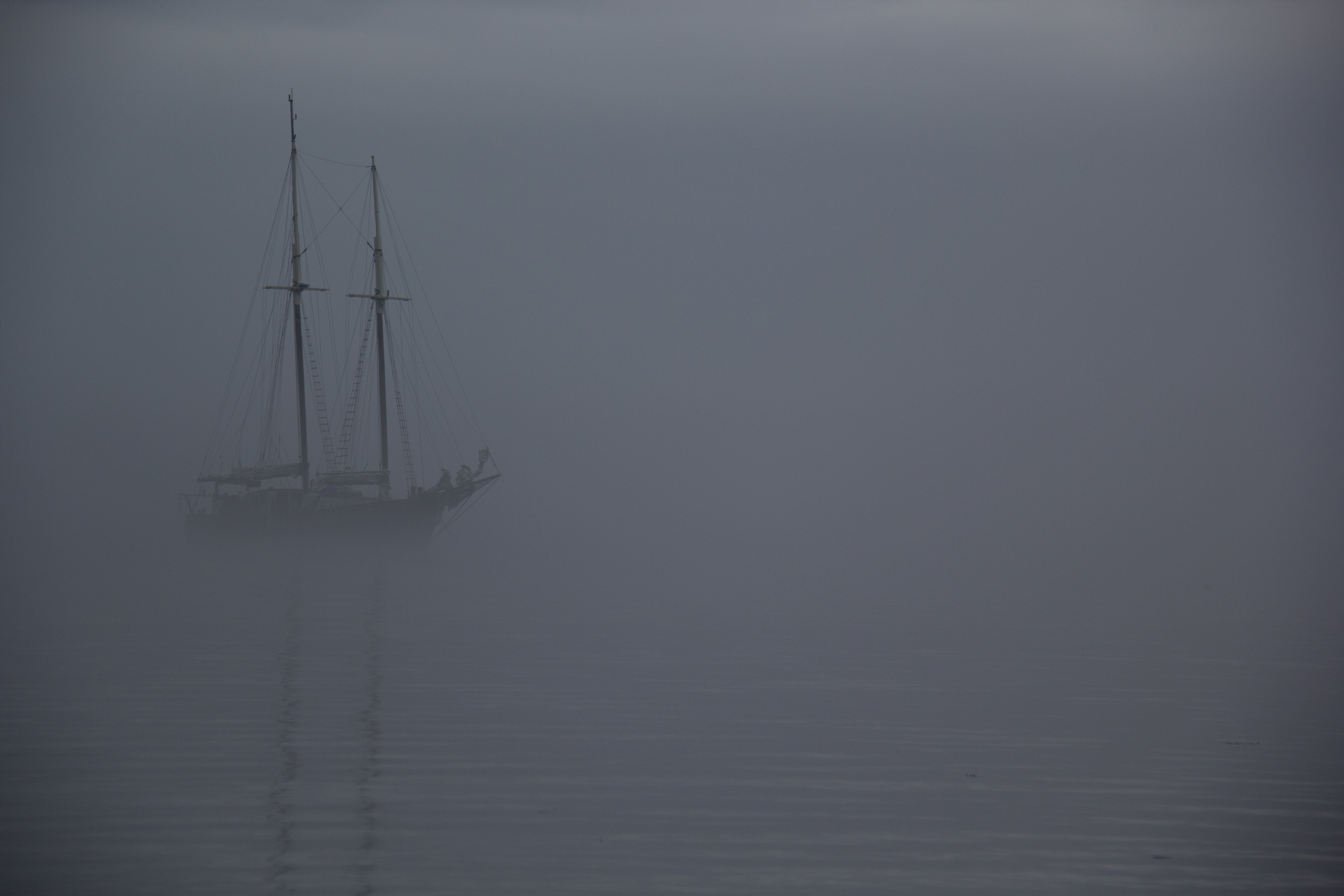 A faint image of a sailboat partially obscured by thick fog on calm waters