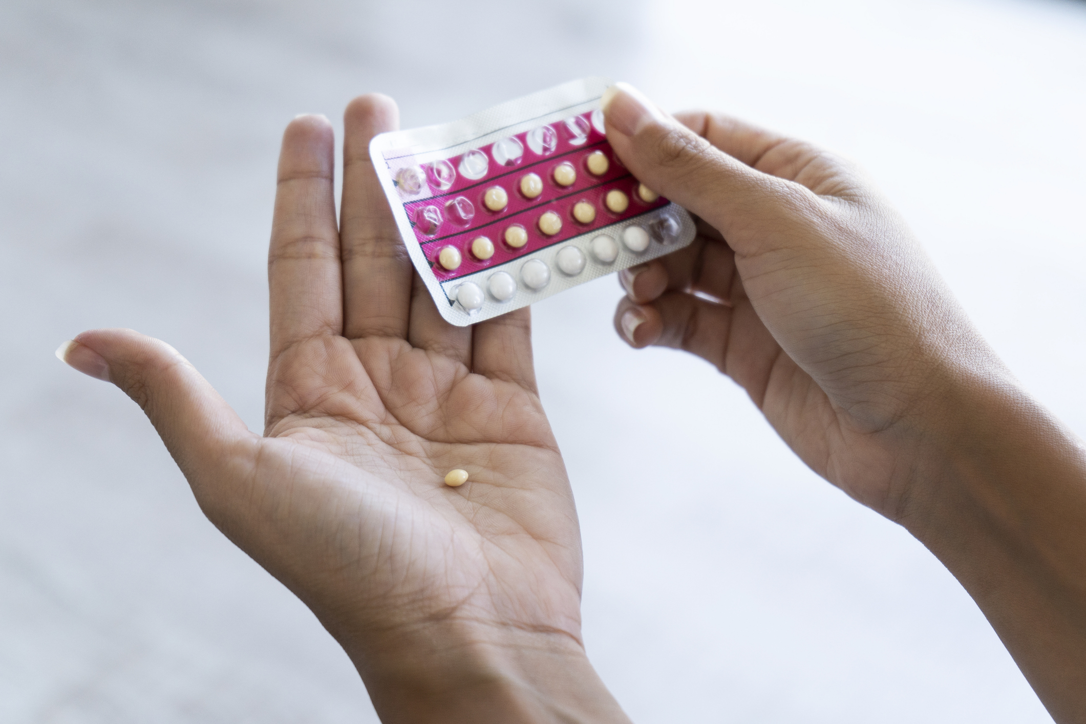 A person holding a pack of birth control pills in one hand and a single pill in the other
