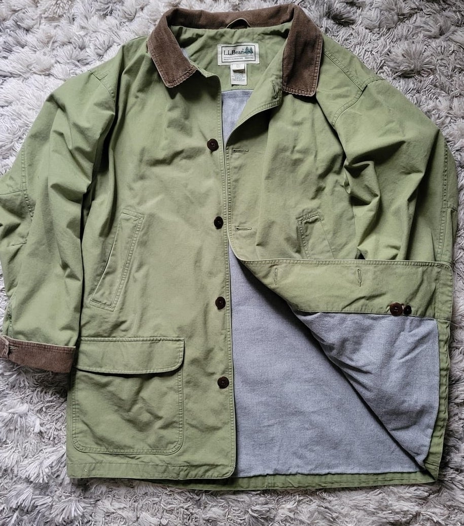 A green barn jacket with brown collar and sleeve accents is laid out on a textured surface, showing its interior lining