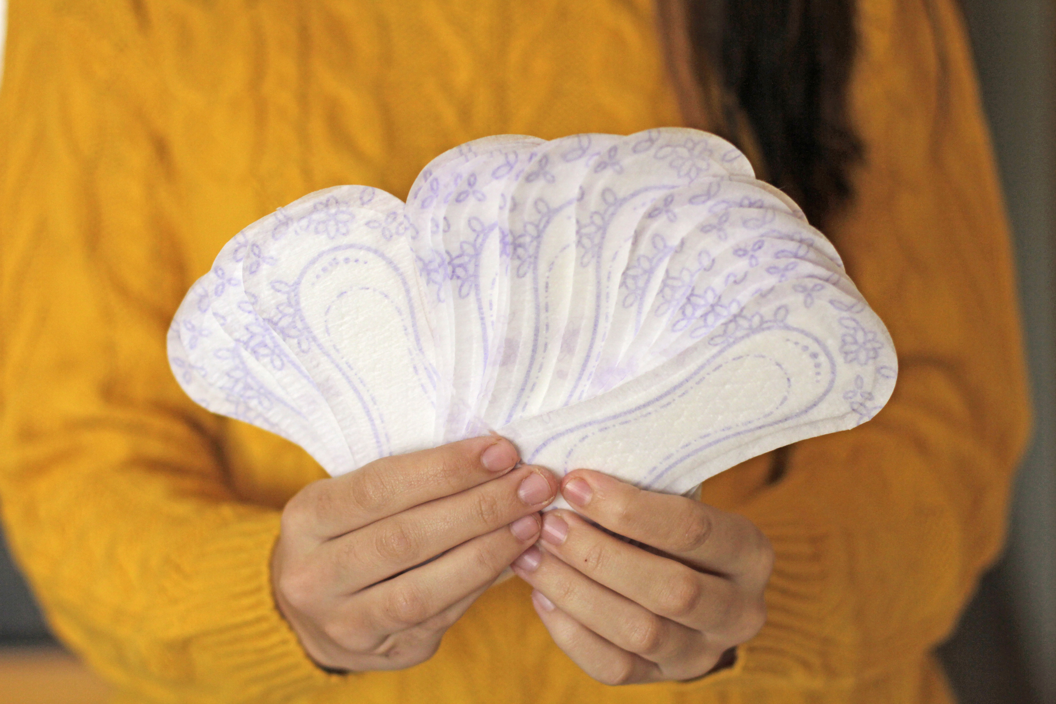 A person holding a fan of menstrual pads with flower patterns, wearing a textured sweater
