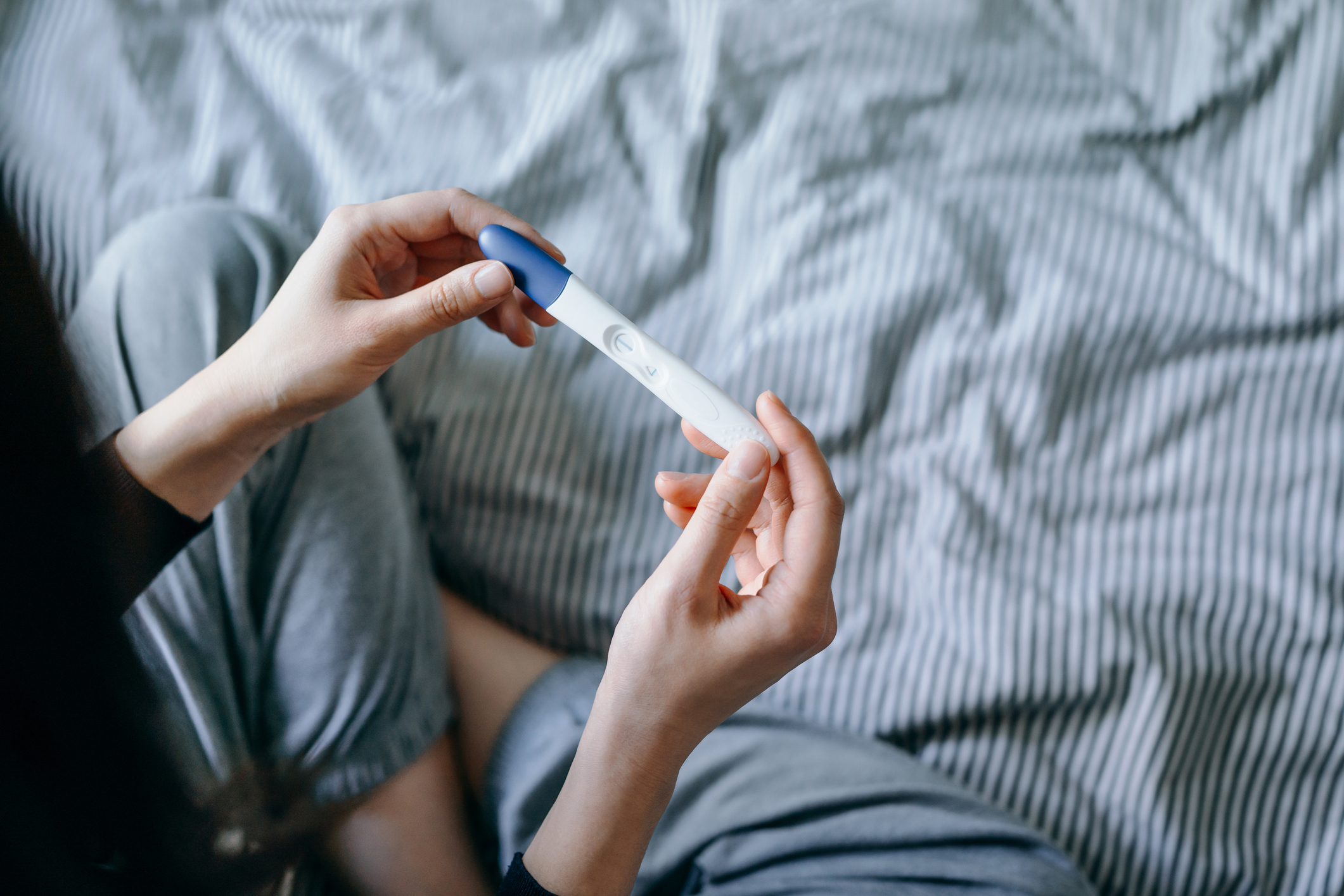 Person holding a pregnancy test while sitting on a bed