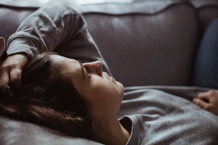 A woman lays on a couch, resting her head on her hand, appearing relaxed and thoughtful