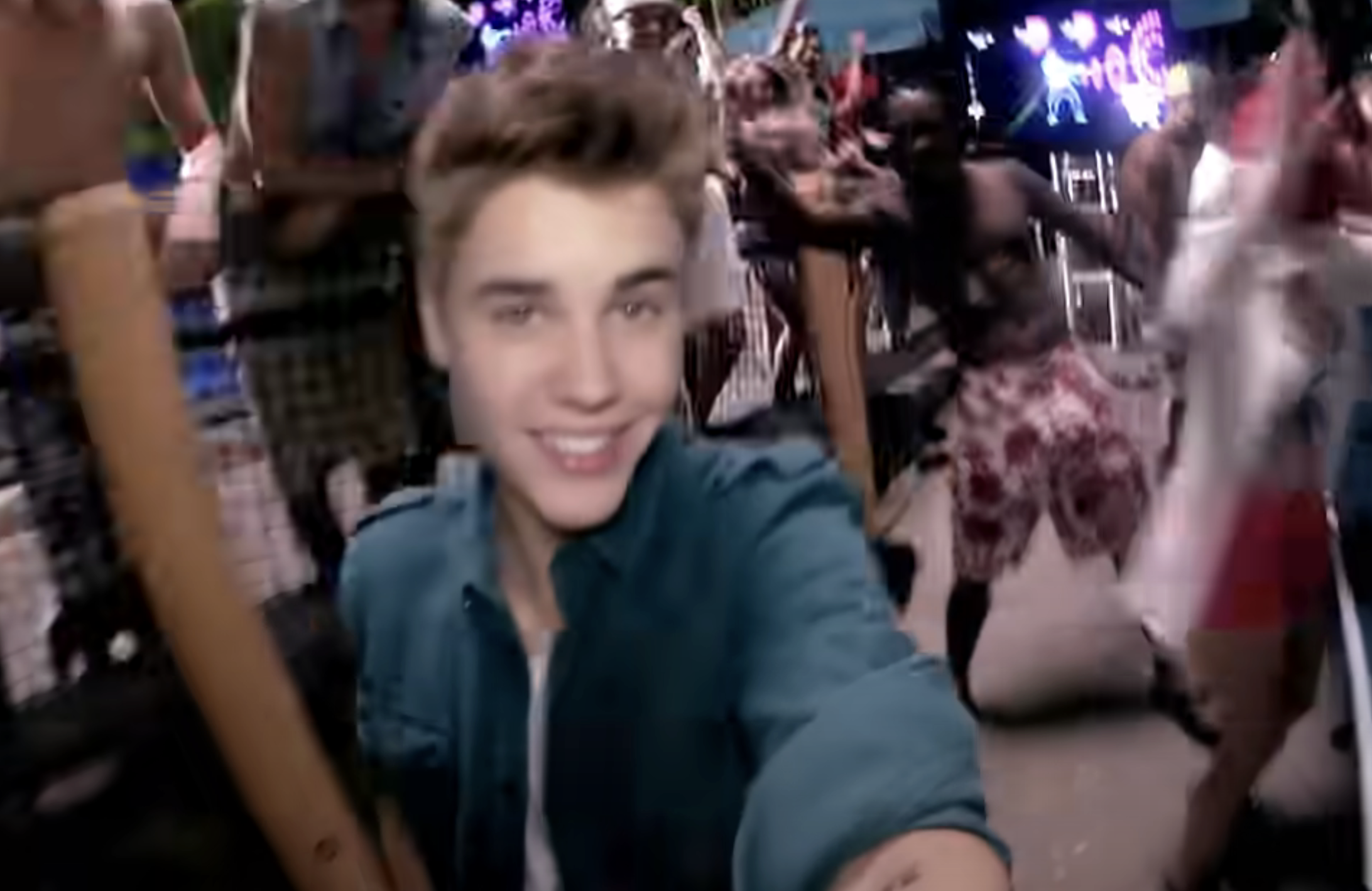 Justin Bieber holding camera from selfie angle at a lively outdoor party with dancing people in the background