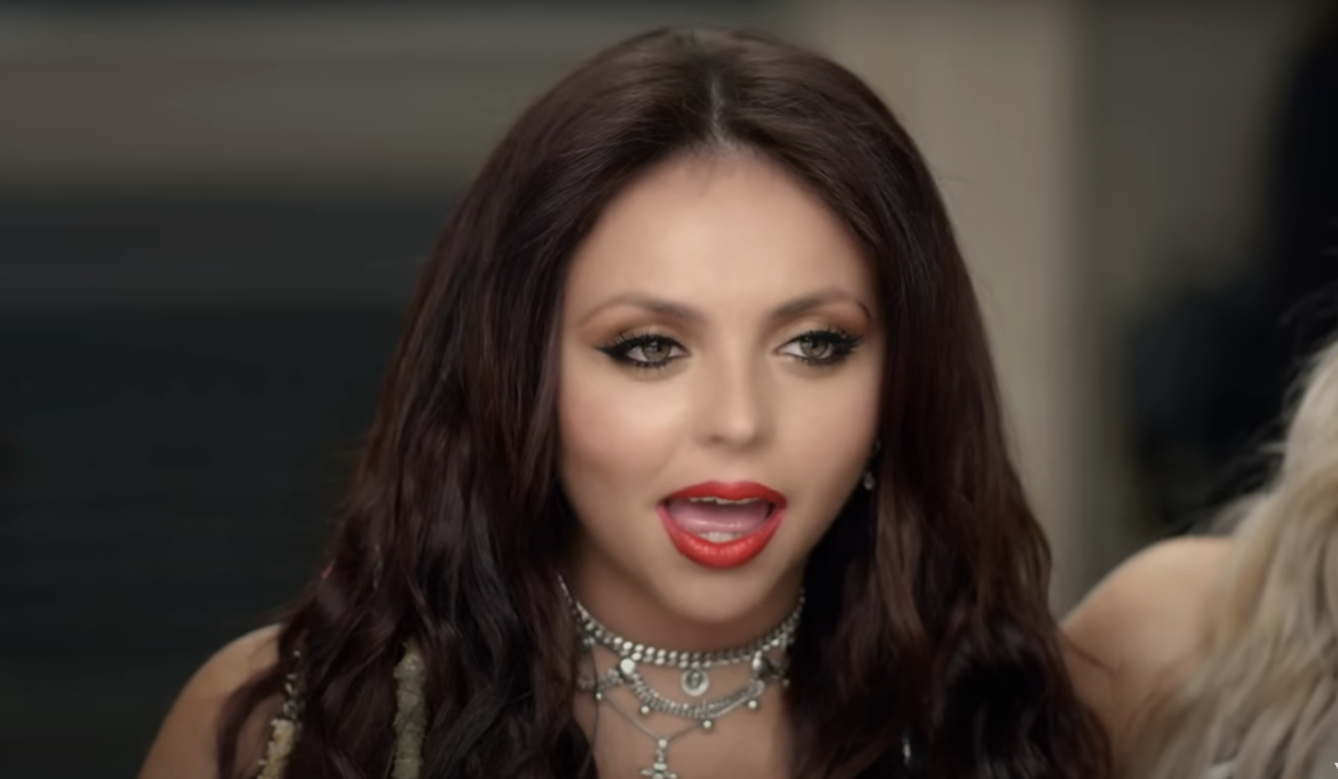 Jesy Nelson, wearing a layered necklace, looking slightly off-camera and wearing a vibrant lipstick