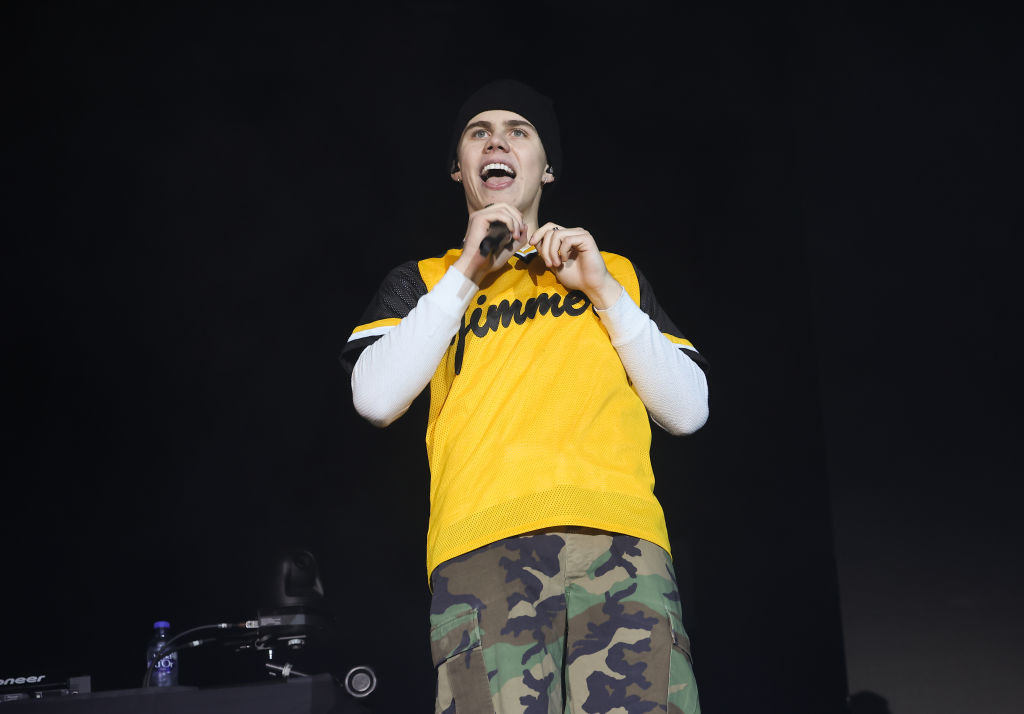 The Kid LAROI performs on stage wearing a birght jersey and camo pants, holding a microphone and smiling