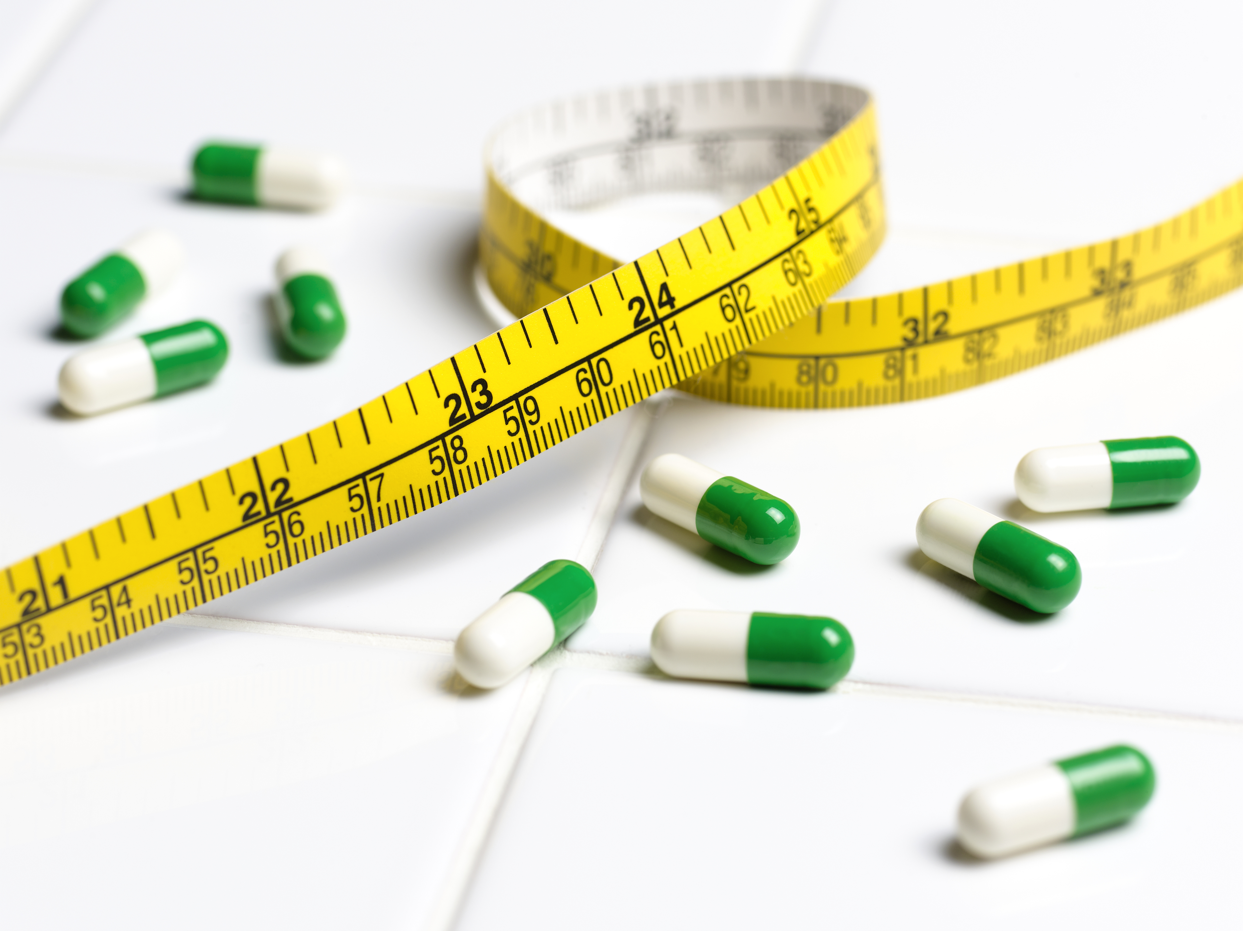 Green and white capsules scattered on a table next to a yellow tape measure