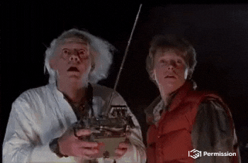 Dr. Emmett Brown wearing a lab coat, and Marty McFly in a puffy vest, stare in amazement while holding a remote control device