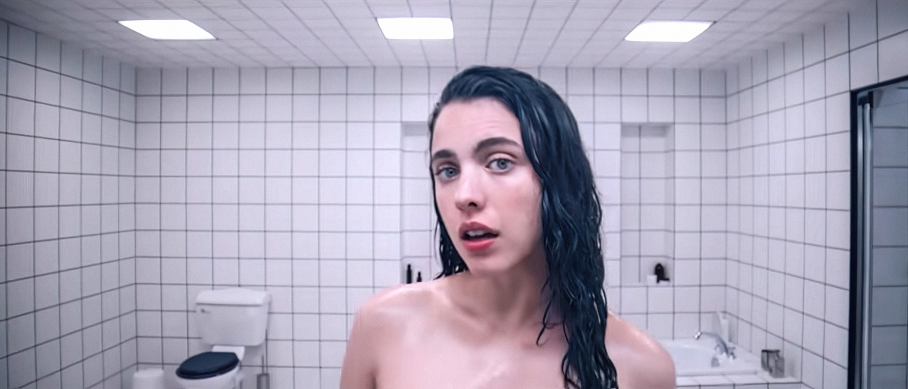 Margaret Qualley stands in a bathroom with wet hair, looking at the camera, with tiled walls and bathroom fixtures visible in the background