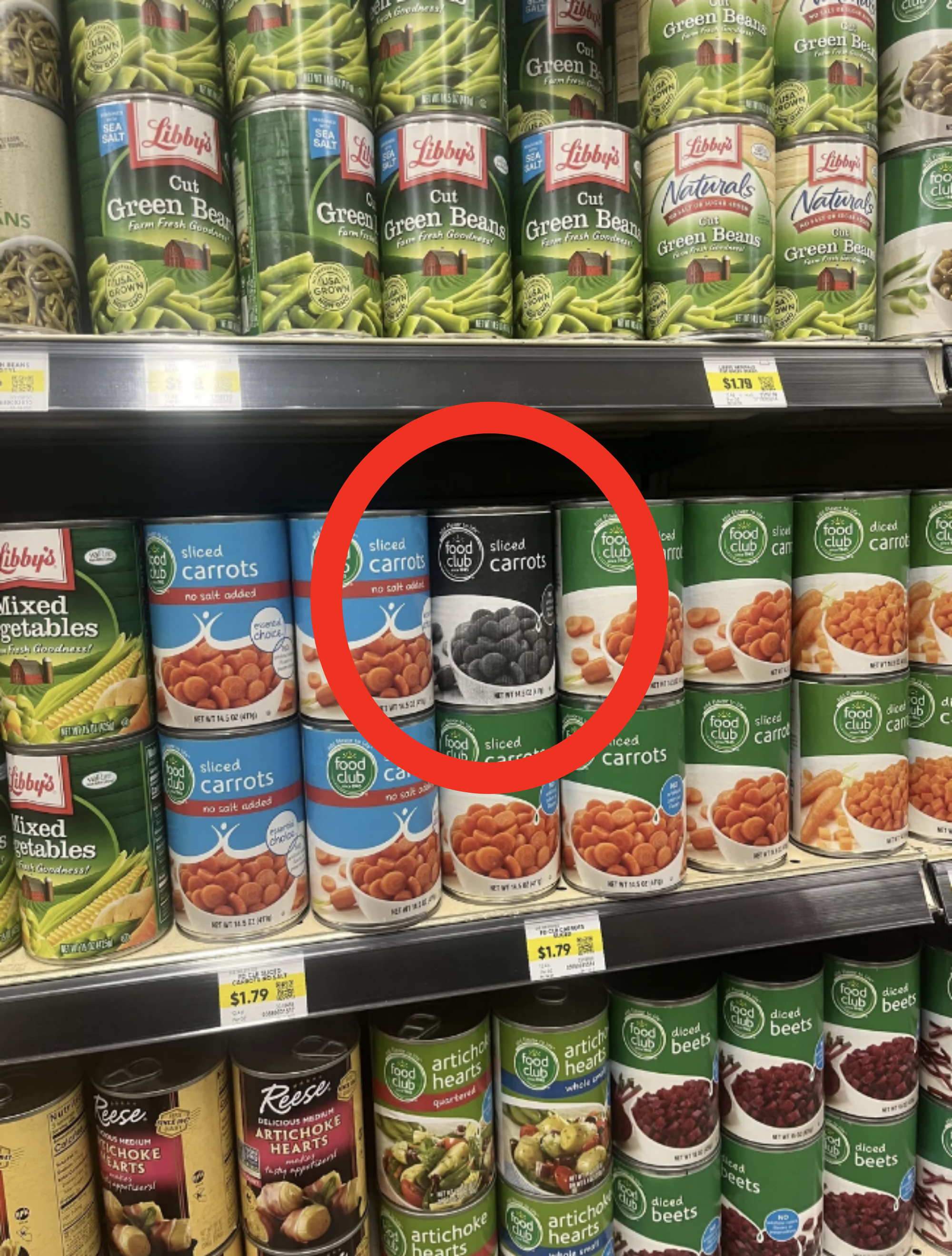 Canned vegetables on a grocery store shelf, including Libby's green beans, mixed vegetables, and sliced carrots, as well as various other brands and types