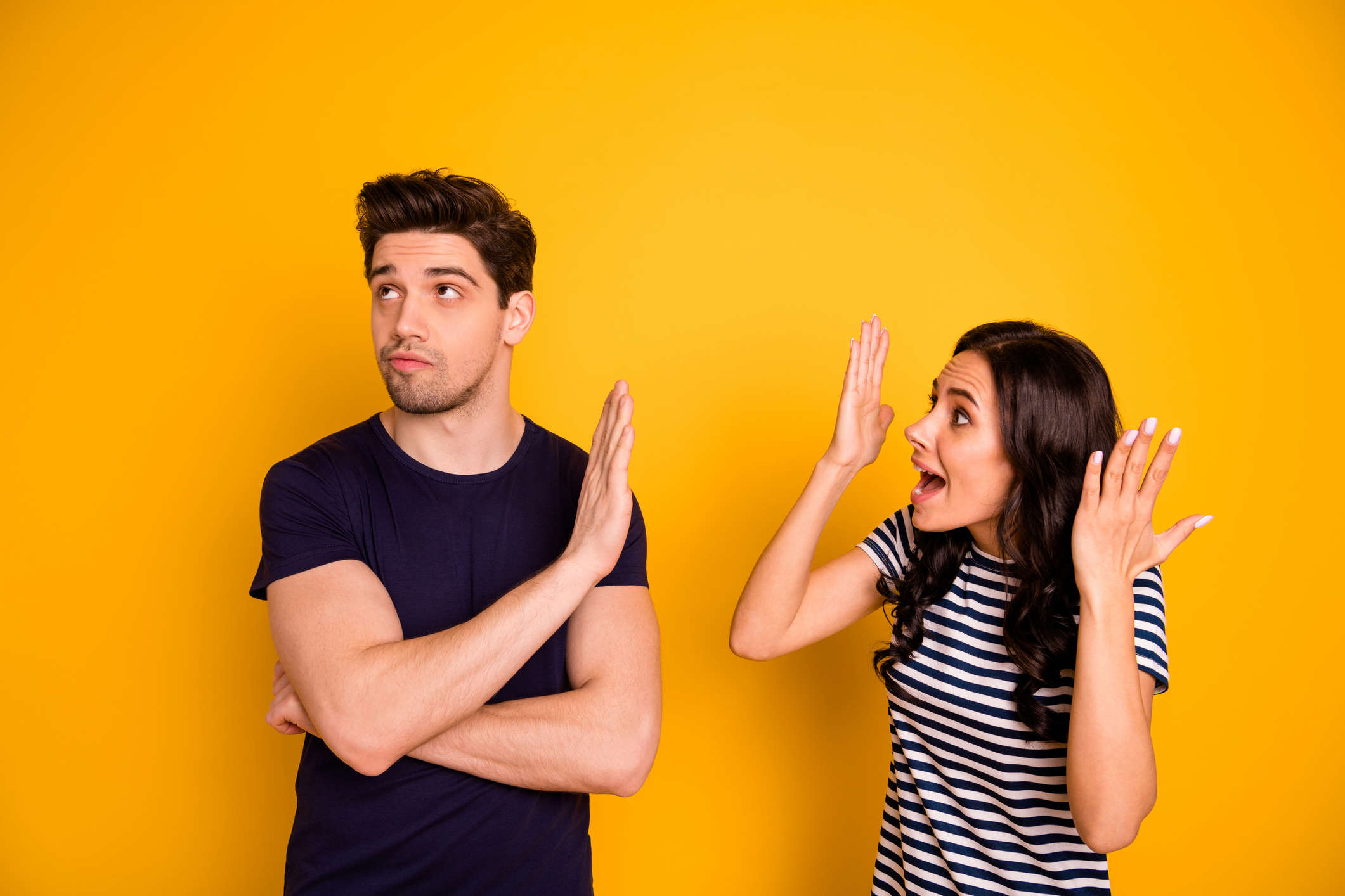 A man with a disinterested expression and a woman looking surprised or frustrated have an animated discussion against a yellow background
