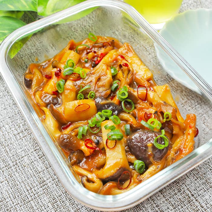 ガラス容器に盛られたきのこ。刻みねぎとか赤唐辛子がトッピングされている。