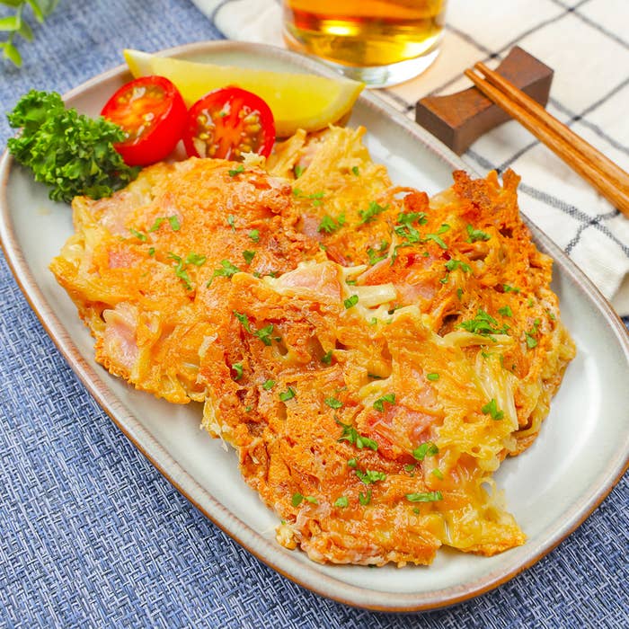 長方形の皿に並べられた美味しそうな料理。横にミニトマト、レモン、パセリが添えられ、箸とビールが背景にある。