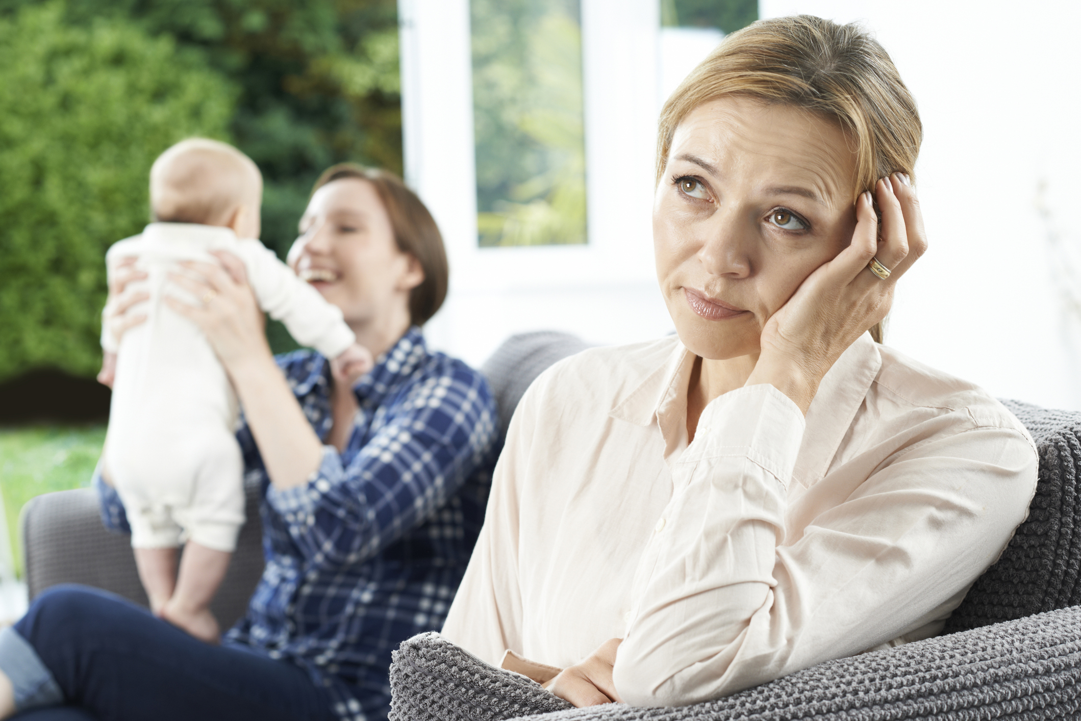 Two women with a baby; one woman joyfully plays with the baby, while the other looks tired and contemplative