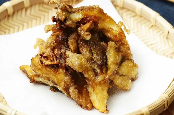 竹のバスケットに盛り付けられた舞茸の天ぷら。木製のテーブルに置かれている。