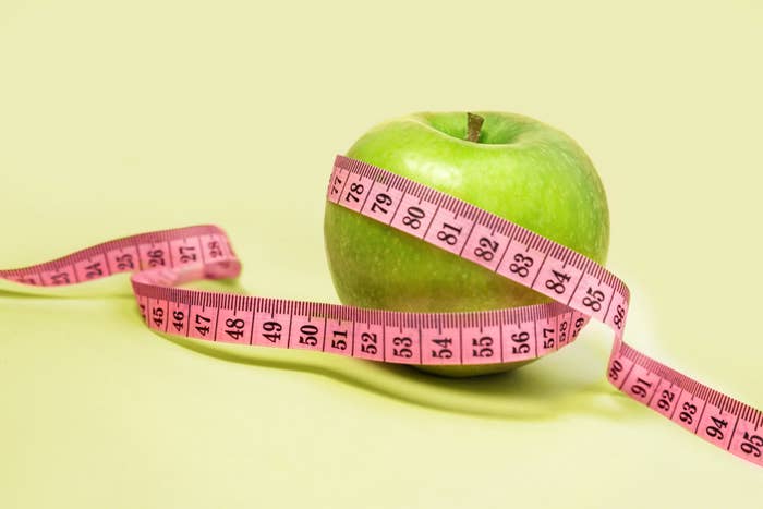 A green apple wrapped with a pink measuring tape symbolizing health and fitness