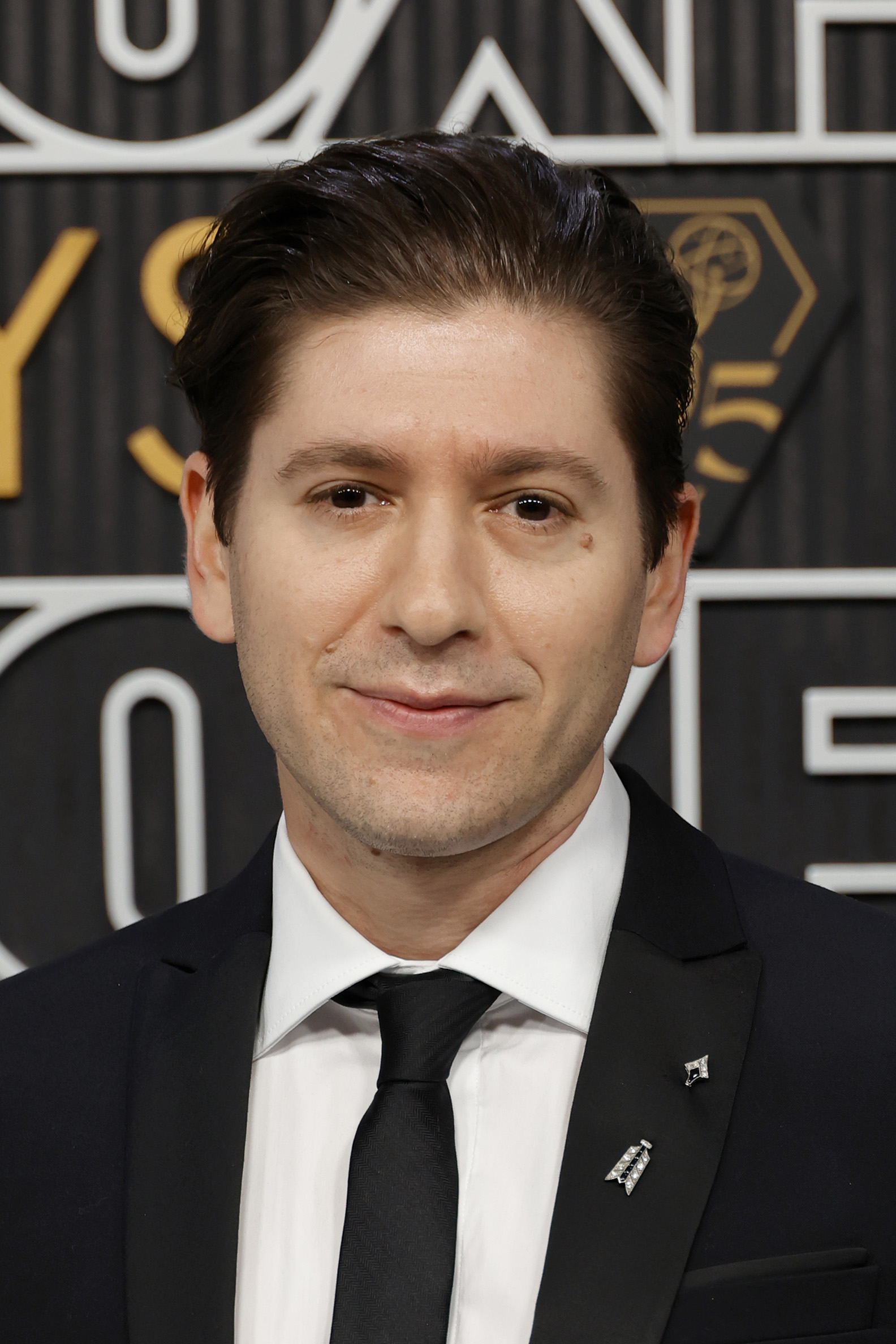Michael Zegen on the red carpet in formal attire with a black suit, white shirt, and black tie