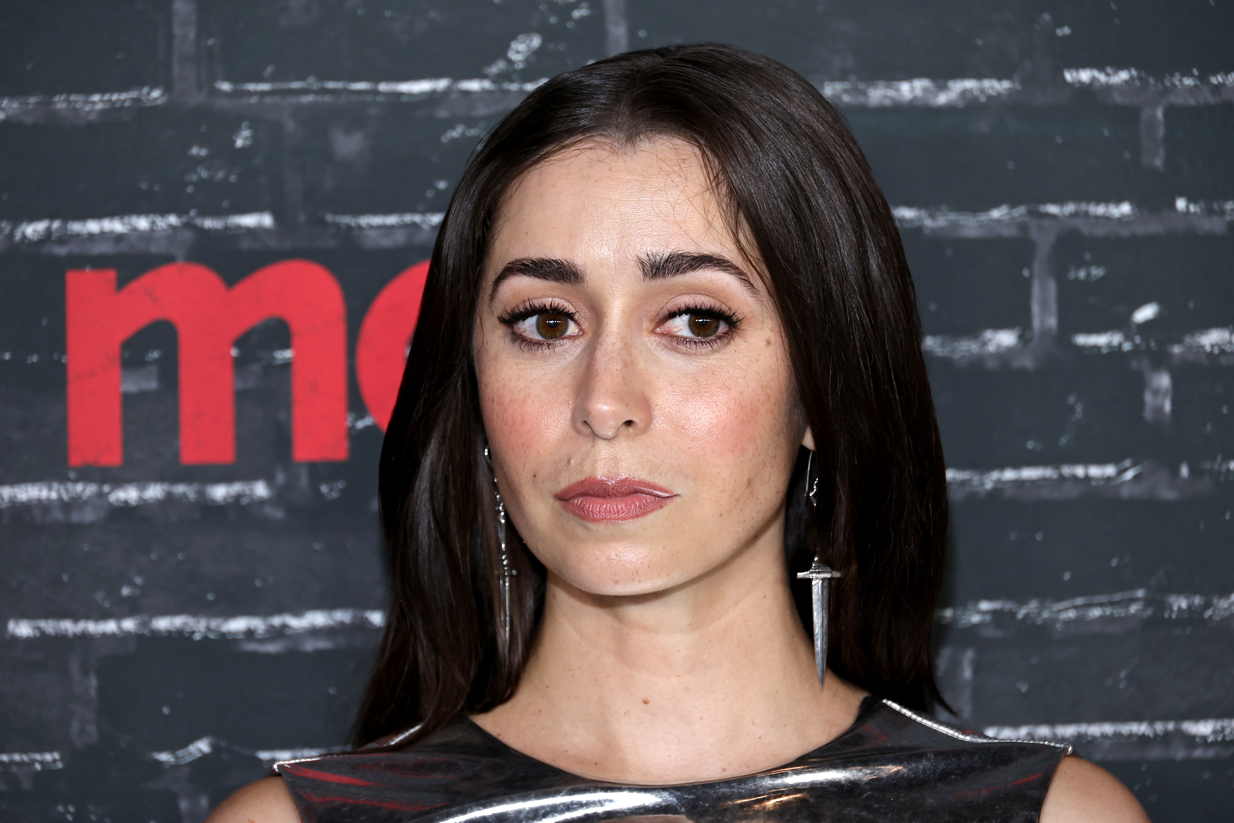 Cristin Milioti at a red carpet event, wearing silver earrings and a sleek, reflective dress