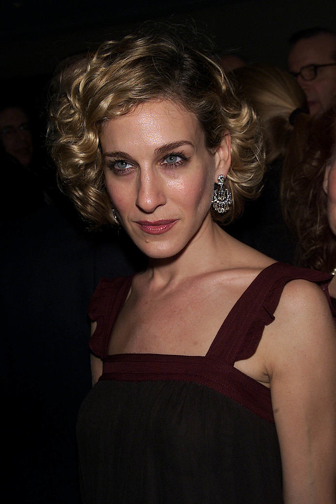 Sarah Jessica Parker in a sleeveless dress with intricate earrings, posing at a formal event, with a shirt, curly bob